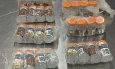 Muitos frascos de vidro com tampas laranja, alguns com rótulo 'T.G.' e códigos QR, embrulhados em plástico