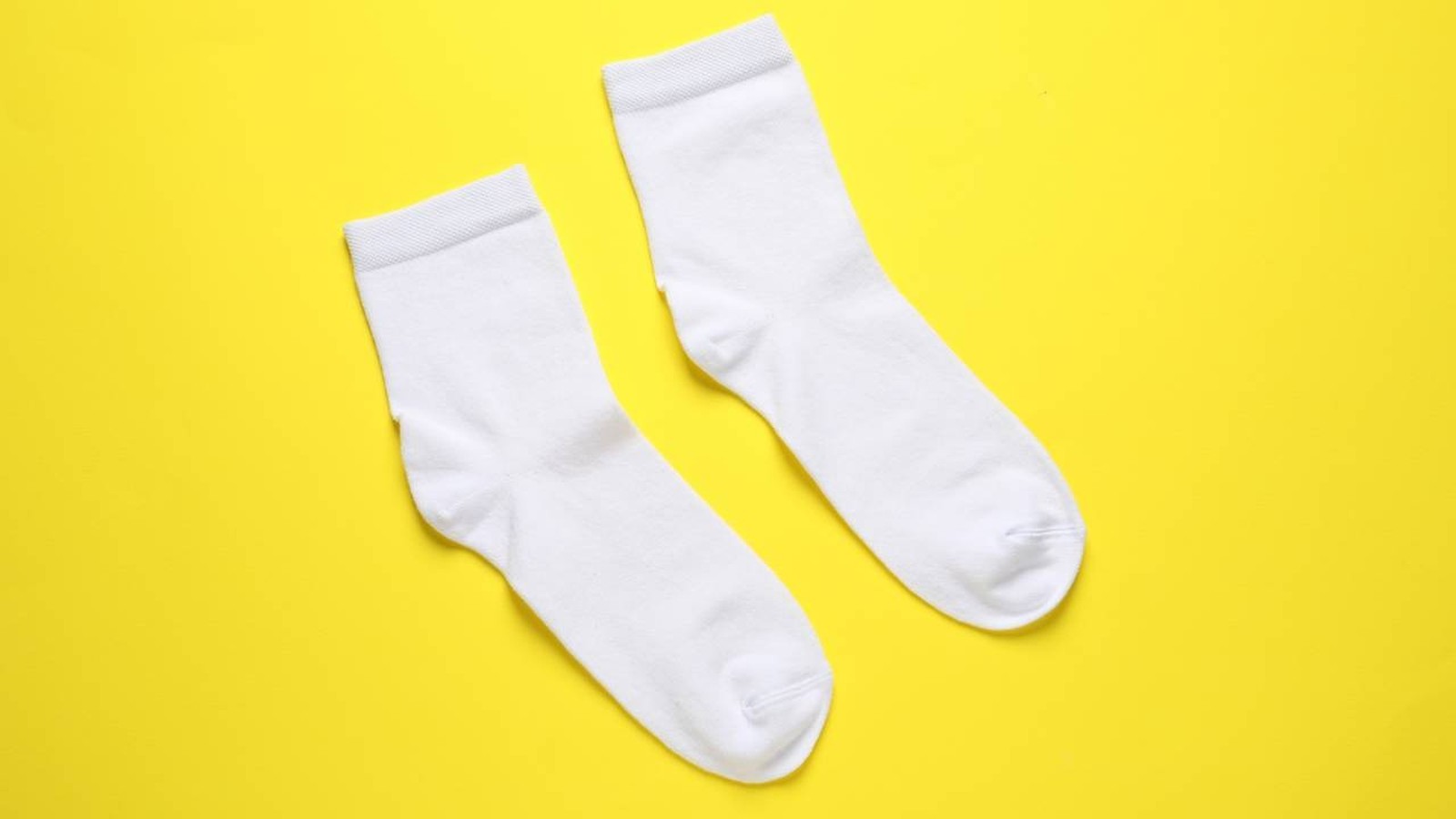 Duas meias brancas limpas e lisas sobre um fundo amarelo vibrante