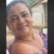 Mulher Hélia das Chagas Barbosa sorrindo levemente, com brincos e blusa roxa, fundo externo desfocado