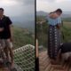 Jovem casal em varanda. Homem ajoelhado no chão de rede, mulher olha para baixo com montanhas ao fundo