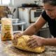 Mulher sova massa de pão de milho em mesa de madeira rústica, saco de farinha visível