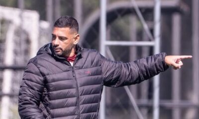 Homem de jaqueta escura e barba, apontando o dedo, em campo de futebol