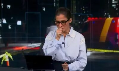 Jornalista Renata Vasconcellos com a mão na boca, tossindo em bancada de telejornal ao vivo.