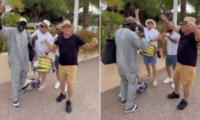 Cantor Leonardo e três homens dançam e gesticulam em rua, ao lado de carrinho de vendas