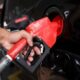 Mão inserindo bico de bomba de combustível em tanque de carro preto, escrito GASOLINA