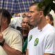 Flávio Bolsonaro, com guarda-chuva, entre apoiadores, incluindo homem com camiseta branca e broches "22"