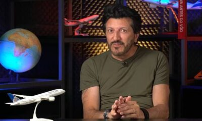 Homem de barba em camiseta verde sentado, com modelo de avião United e globo