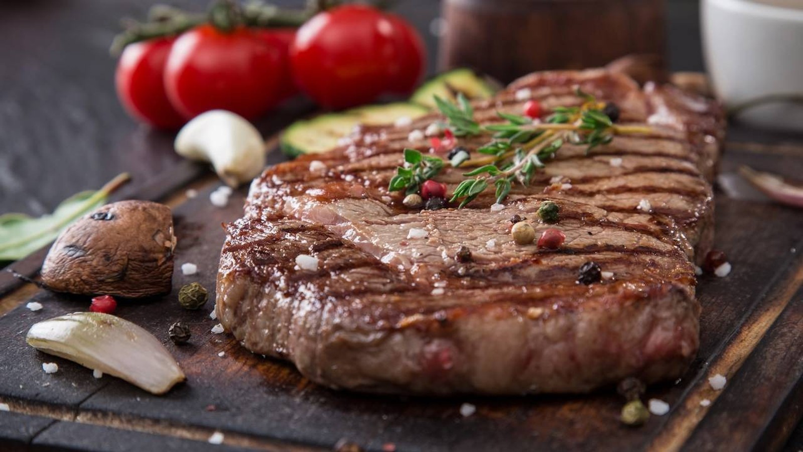 Bife grelhado em tábua de madeira com sal, pimenta, tomilho, tomate, cogumelos e alho no fundo