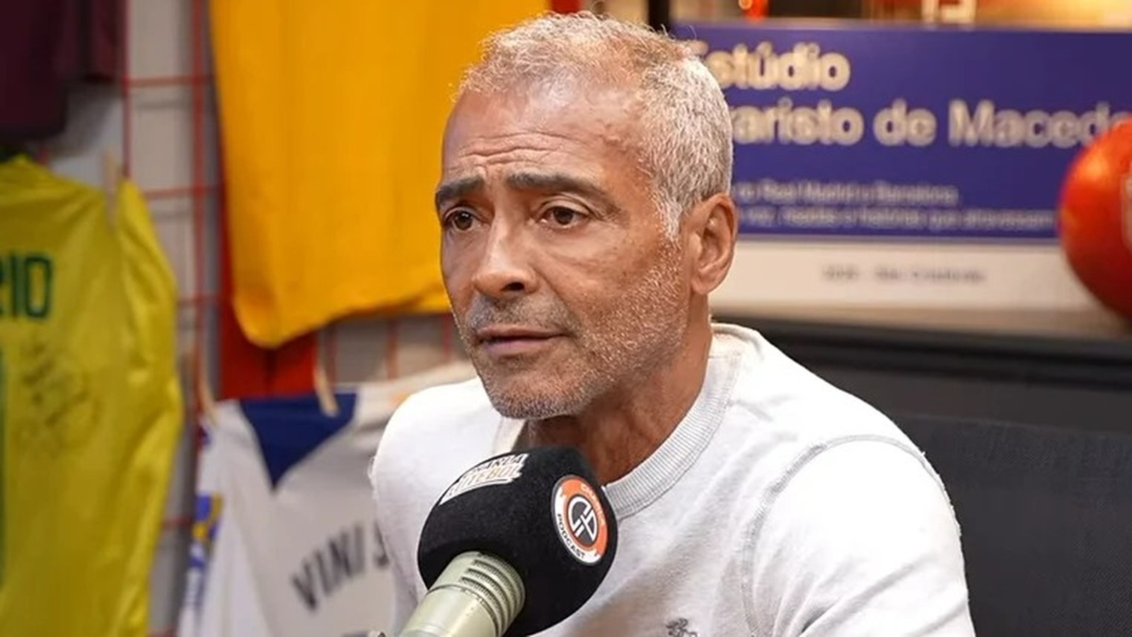 Romário, com cabelo e barba grisalhos, fala em microfone do Charla Podcast em estúdio.