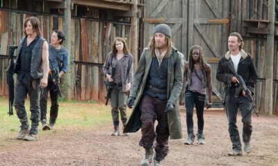 Seis personagens de The Walking Dead, incluindo Rick, Michonne e Daryl, caminham armados em um acampamento
