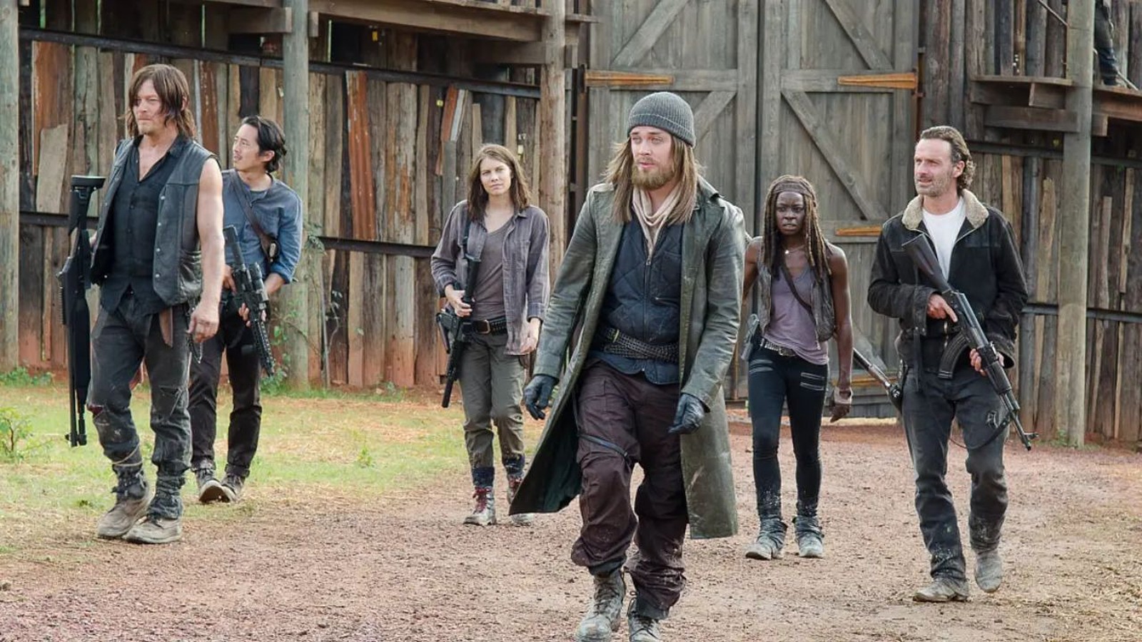 Seis personagens de The Walking Dead, incluindo Rick, Michonne e Daryl, caminham armados em um acampamento