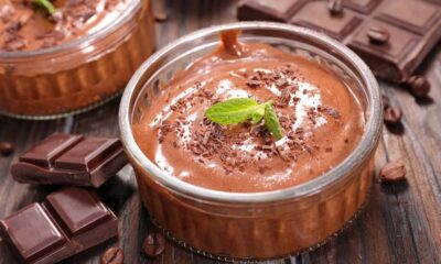 Tigela de mousse de chocolate com raspas e hortelã, barras de chocolate e grãos de café em madeira