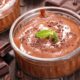 Tigela de mousse de chocolate com raspas e hortelã, barras de chocolate e grãos de café em madeira