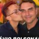 Pessoa jovem beija Flávio Bolsonaro na bochecha, com bandeira arco-íris e do Brasil