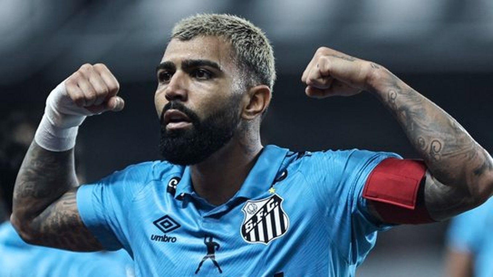 Gabriel Barbosa, camisa azul do Santos, barba e cabelo loiro, flexionando os braços