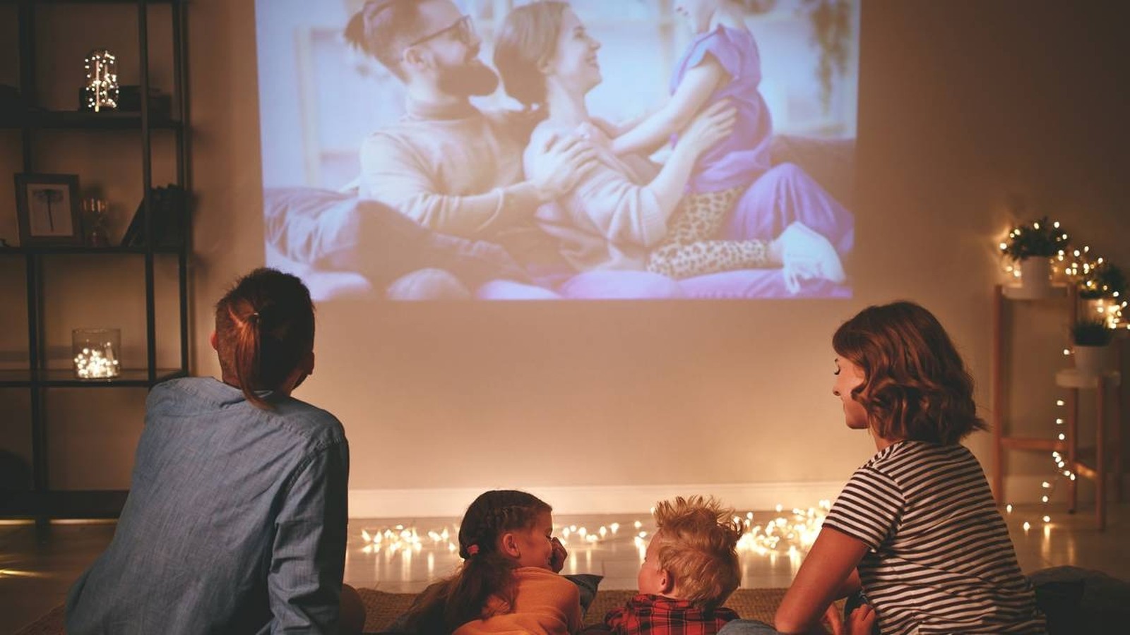 Família assiste a filme projetado na parede de sala escura