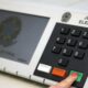 Mão pressiona botão "CONFIRMA" em urna eletrônica brasileira com teclado numérico visível