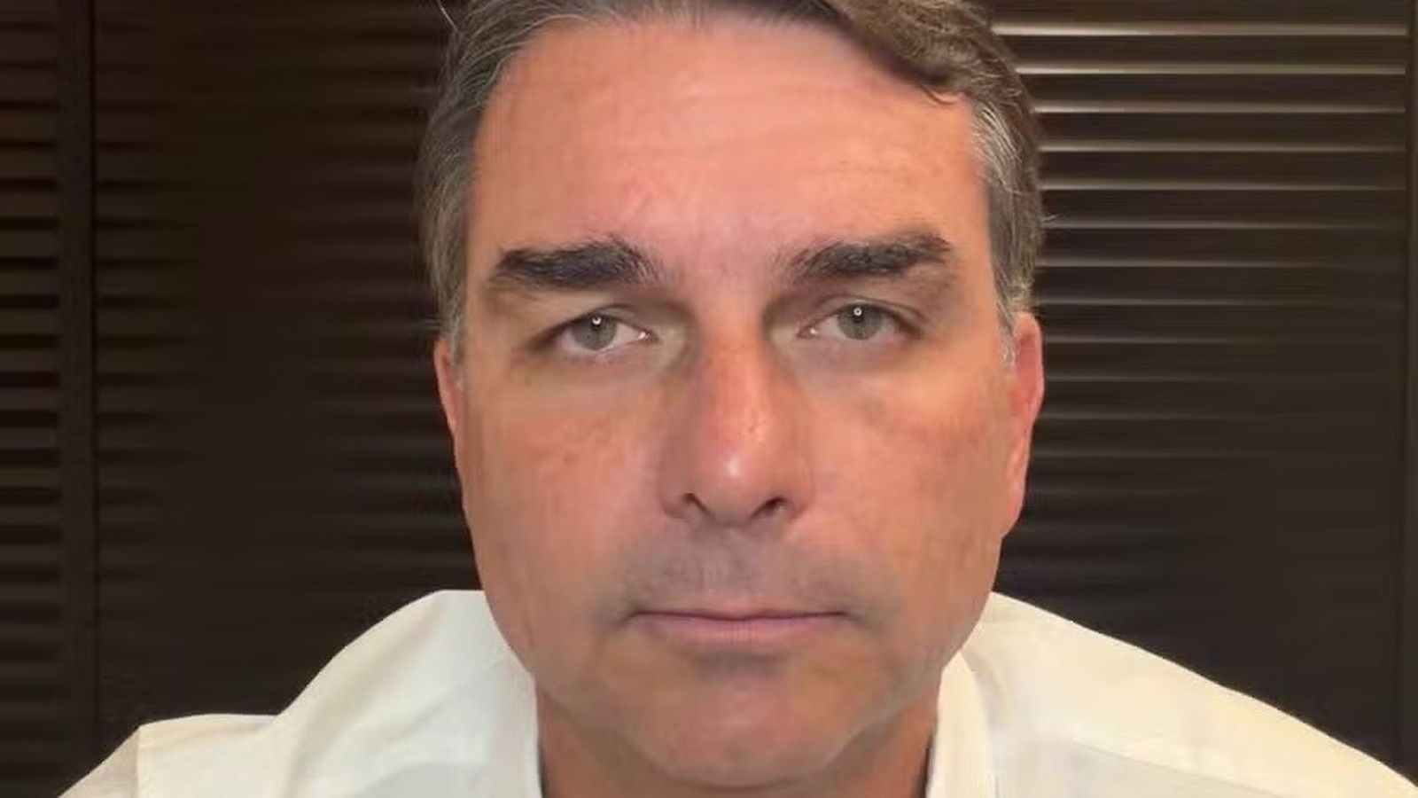 Close-up do senador Flávio Bolsonaro, com expressão neutra, olhando diretamente para frente