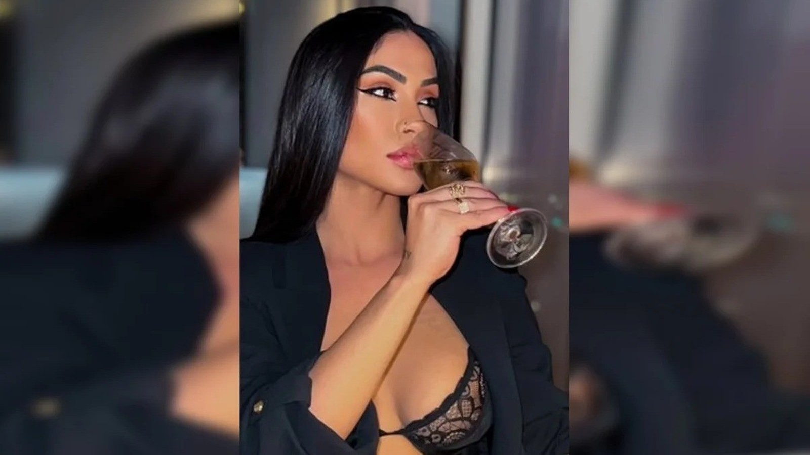 Mulher de cabelos pretos, maquiagem, blazer preto e sutiã, bebendo em taça de vinho