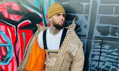 Chris Brown usa gorro amarelo, jaqueta The North Face Gucci, colar, contra parede grafite