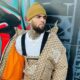 Chris Brown usa gorro amarelo, jaqueta The North Face Gucci, colar, contra parede grafite
