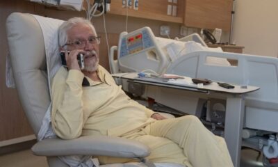 Idoso de pijama amarelo, sentado em poltrona de hospital, falando ao celular
