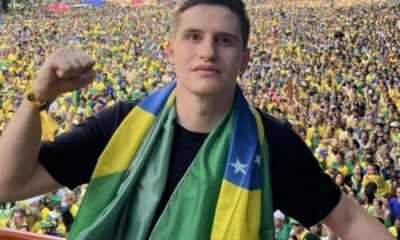 Homem com cachecol da bandeira do Brasil, punho cerrado, à frente de grande multidão