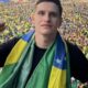 Homem com cachecol da bandeira do Brasil, punho cerrado, à frente de grande multidão