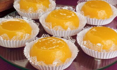 Seis quindins amarelos brilhantes em forminhas brancas de papel rendado sobre uma bandeja de vidro