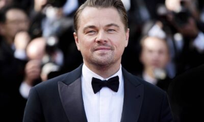 Leonardo DiCaprio em close-up, sorrindo levemente, vestindo terno preto e gravata borboleta