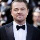 Leonardo DiCaprio em close-up, sorrindo levemente, vestindo terno preto e gravata borboleta