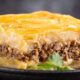 Fatia de escondidinho: purê de batata, carne moída, queijo em prato escuro