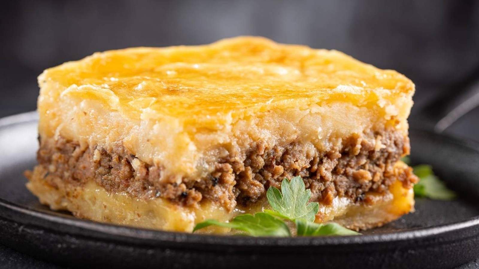 Fatia de escondidinho: purê de batata, carne moída, queijo em prato escuro