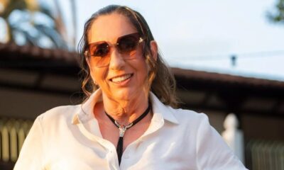 Margareth Serrão sorrindo, usando óculos escuros, camisa branca e colar com adorno prateado