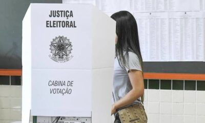 Mulher em cabine de votação com os dizeres "Justiça Eleitoral" e "Cabina de Votação"
