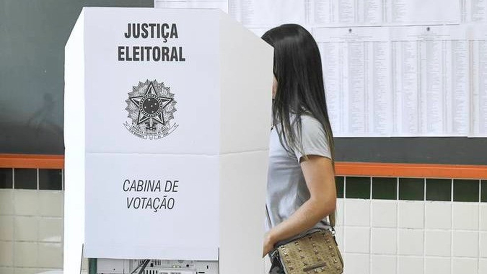 Mulher em cabine de votação com os dizeres "Justiça Eleitoral" e "Cabina de Votação"