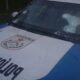 Viatura policial branca e azul com para-brisa e capô perfurados por tiros, logo PMERJ