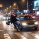Homem inclinado, mochila voando, perto de carro em faixa de pedestres, rua molhada à noite