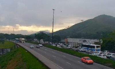 Rodovia com tráfego intenso e congestionamento, veículos parados, montanhas e céu nublado ao fundo