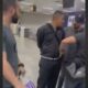 Quatro homens em um aeroporto. Um homem de blusa preta é contido por outros dois