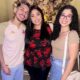 Três pessoas sorrindo: um jovem de barba, uma mulher de blusa floral e uma jovem de óculos