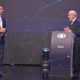Dois homens em trajes formais em um palco de debate, com um pódio escrito "LULA"