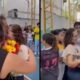Duas mulheres se abraçam em quadra escolar. Alunos observam ao fundo. Camisa tem "ANA.LIGO 23" escrito