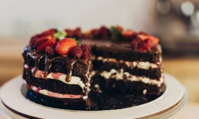 Bolo de chocolate com camadas, recheio branco/rosa, calda, morangos, framboesas, uma fatia removida
