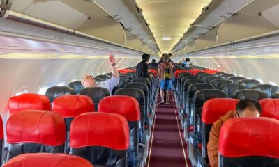 Interior de aeronave AirAsia com assentos vermelhos e pretos, passageiros e compartimentos de bagagem abertos