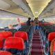 Interior de aeronave AirAsia com assentos vermelhos e pretos, passageiros e compartimentos de bagagem abertos