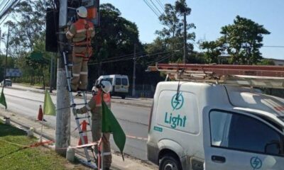 Dois eletricistas da Light em escadas consertam fiação em poste com van de serviço