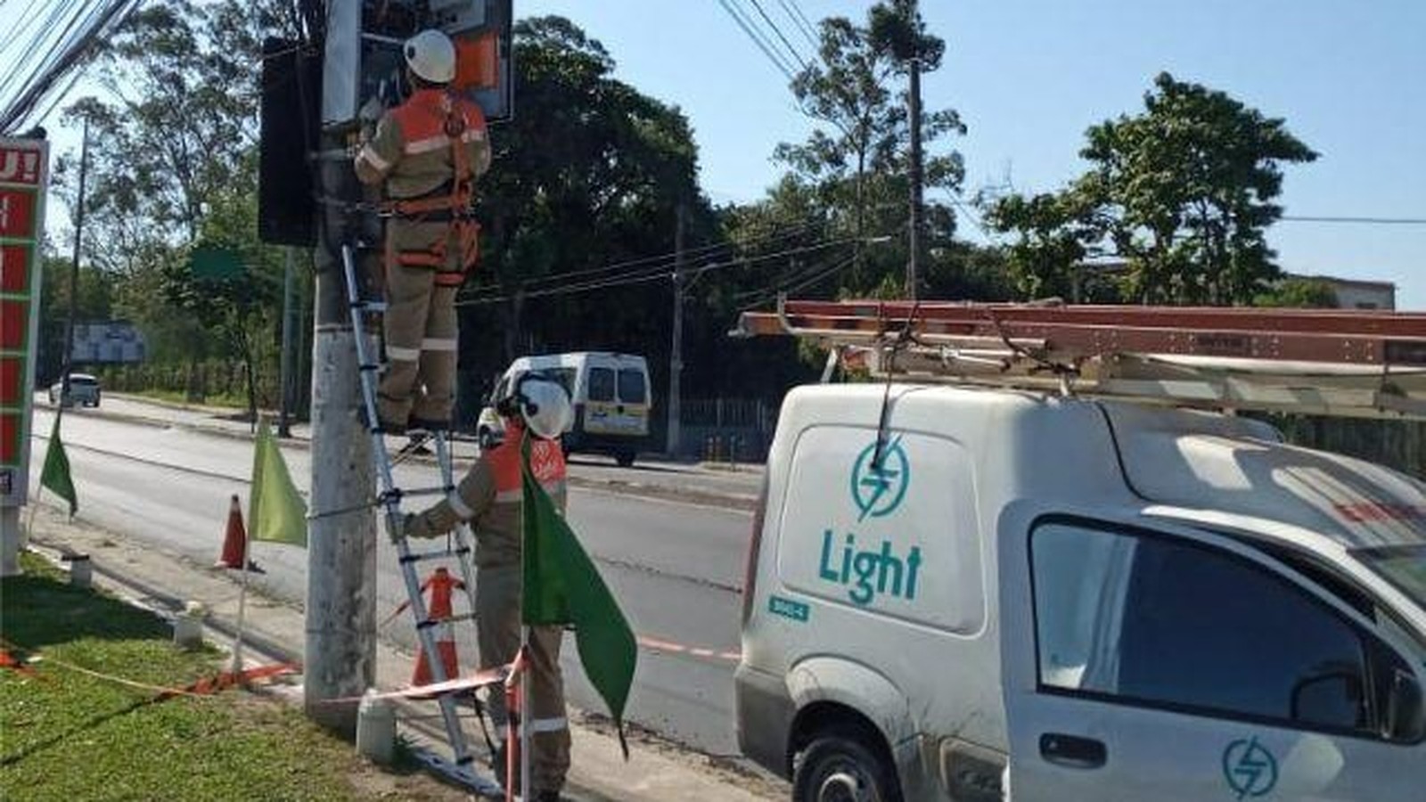 Dois eletricistas da Light em escadas consertam fiação em poste com van de serviço