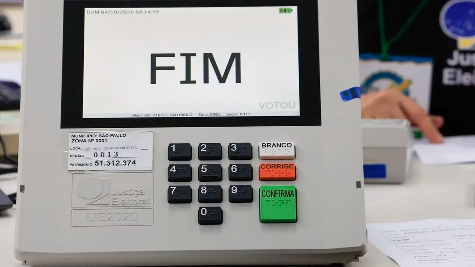 Urna eletrônica exibe "FIM" na tela, teclado numérico e botões Branco, Corrige, Confirma.