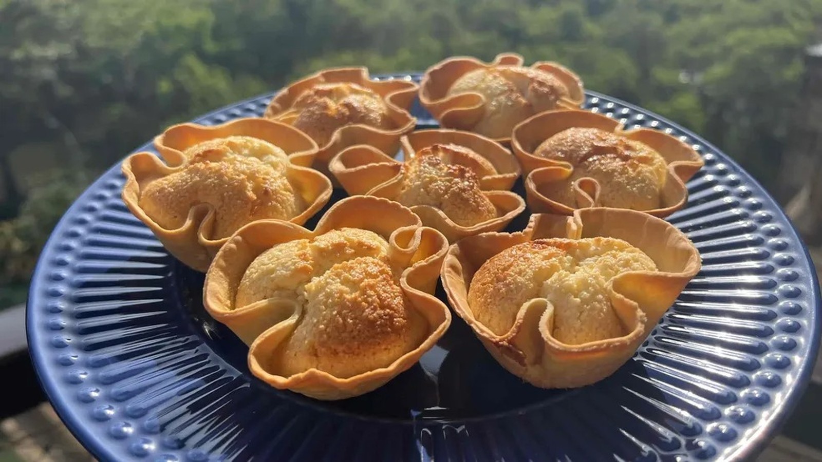 Cestinhas de coco assadas em forma de flor, com recheio claro e casquinha dourada, sobre prato azul